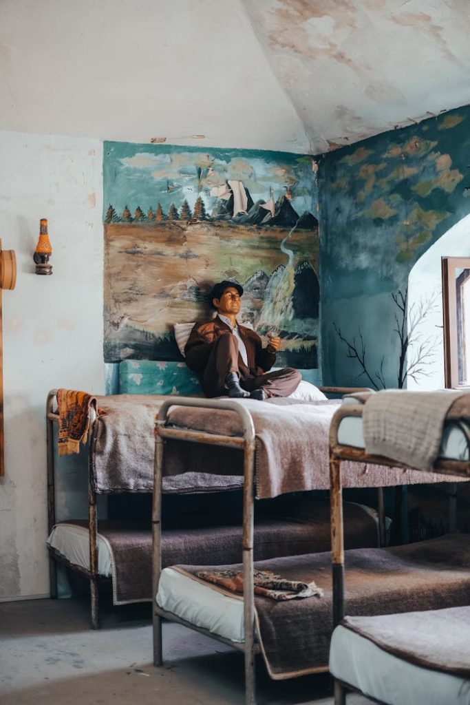 A man sits on a bunk bed in a vintage-style room with artistic wall paintings, adding a cozy touch.